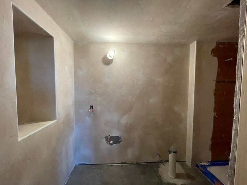 Bathroom interior during construction, featuring unfinished walls, plumbing fixtures, and a recessed shelf.