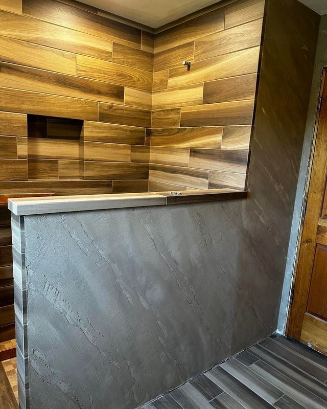 Shower with wood-look tile walls, gray textured half-wall, and matching floor tiles.