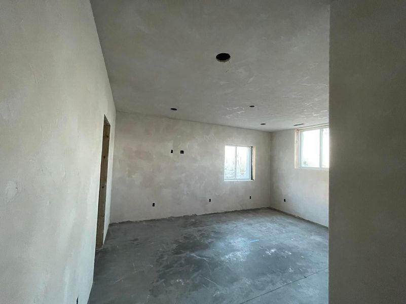 Empty room under construction with concrete floor, unfinished walls, and windows.