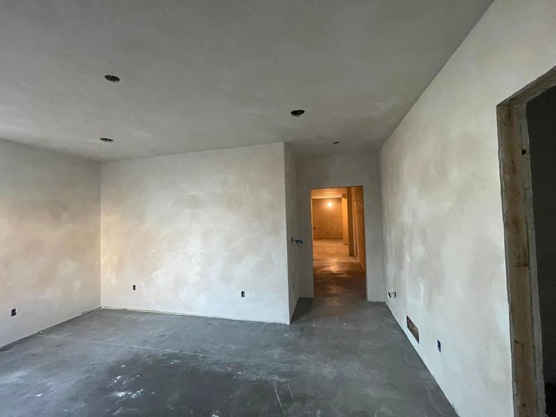 Empty room with textured white walls, concrete floor, and recessed lighting. A doorway leads to a hallway.