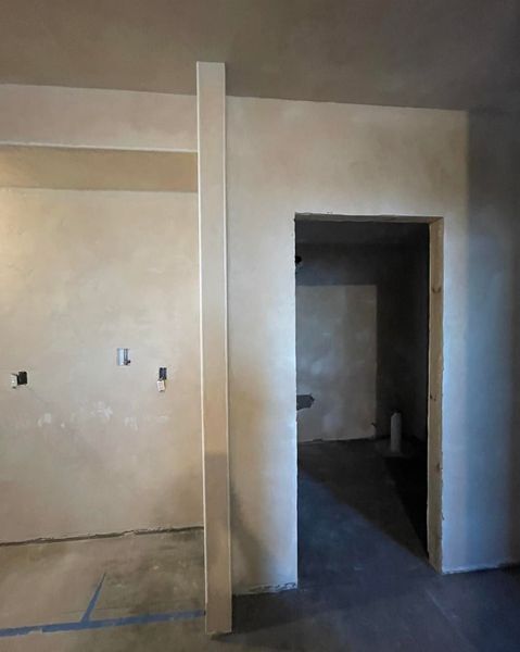 Interior view of a room under construction with a doorway and a vertical pillar. Walls are light-colored.