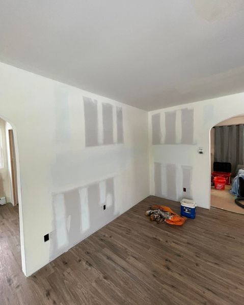 Interior room with drywall patches on white walls, brown flooring, and an arched doorway.