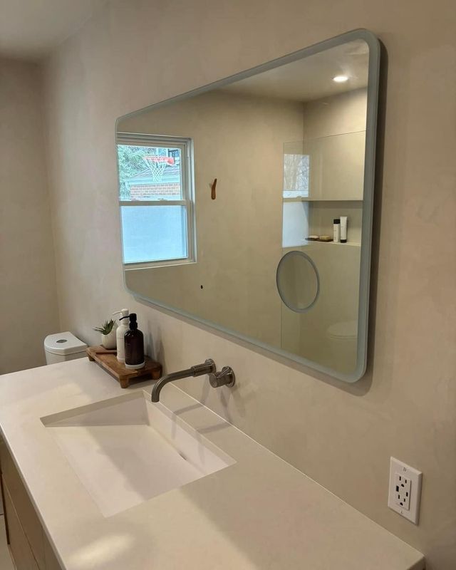 Bathroom with large rectangular mirror above a white sink, and window.