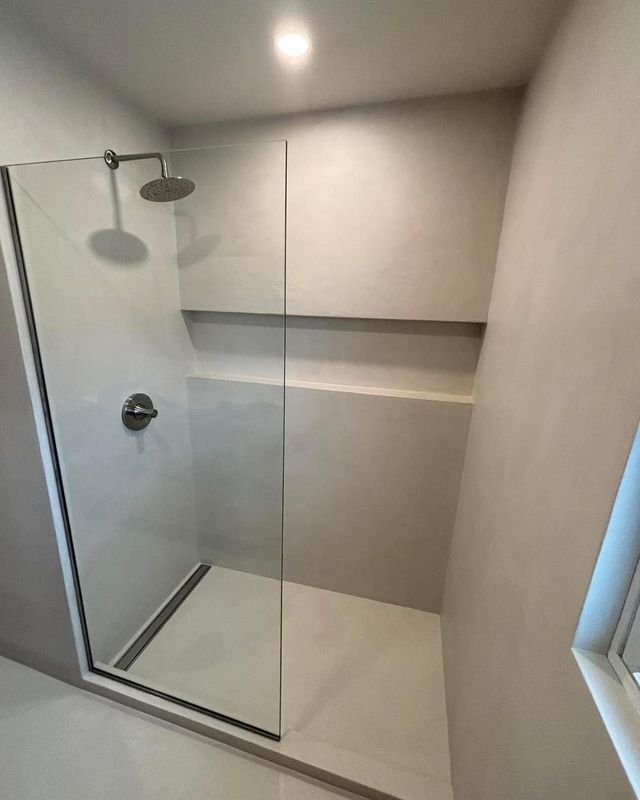 Shower with glass door, gray walls, built-in shelf, and rain showerhead.