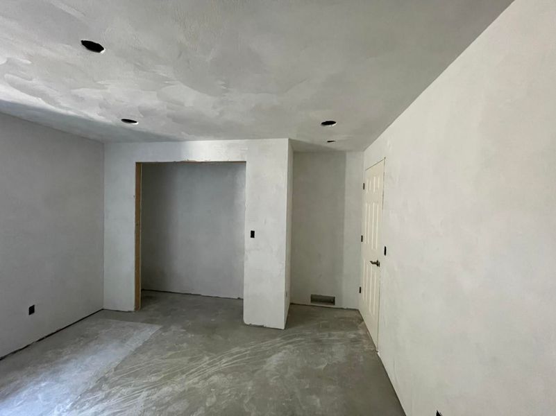 Empty room with unfinished walls, ceiling, and floor, with recessed lighting.