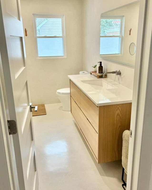 Modern bathroom with light oak floating vanity, white walls, and bright white floors.