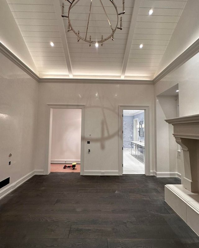 Room with dark wood floors, white walls, and a recessed ceiling with a chandelier. Two doorways.