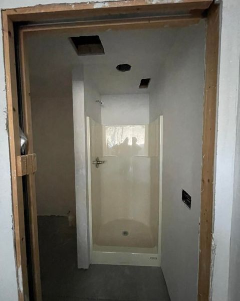 Bathroom undergoing renovation, with a shower stall visible. Open doorway, unfinished walls, and exposed framing.