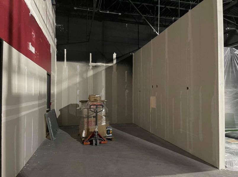 Construction site with unfinished drywall walls; hand truck with boxes in the center, red wall section.