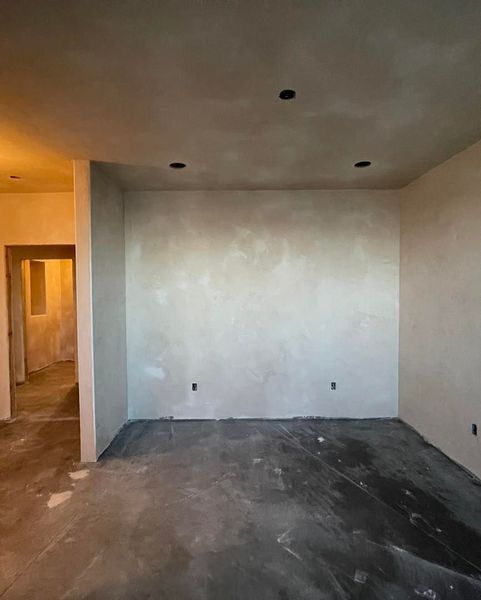 Interior view of a room under construction with gray textured walls, recessed lights, and a concrete floor.