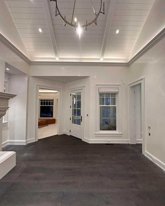 An empty room with dark wood floors, white walls and ceiling, and a chandelier.