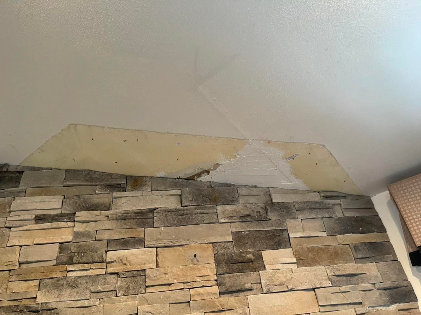 Stone fireplace with a portion of drywall patched in, beneath a white ceiling.
