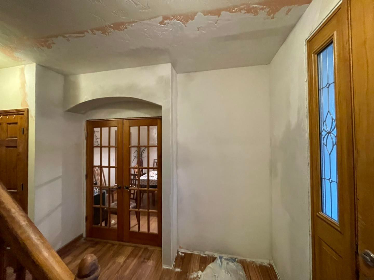 Interior view: hallway with wooden doors, an arched doorway, white walls, and a staircase.