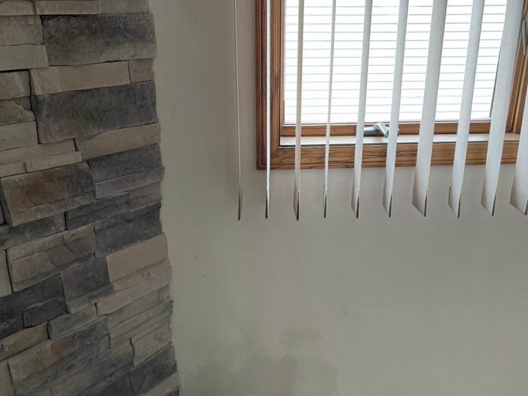 Stone wall next to window with vertical blinds, light shining through.