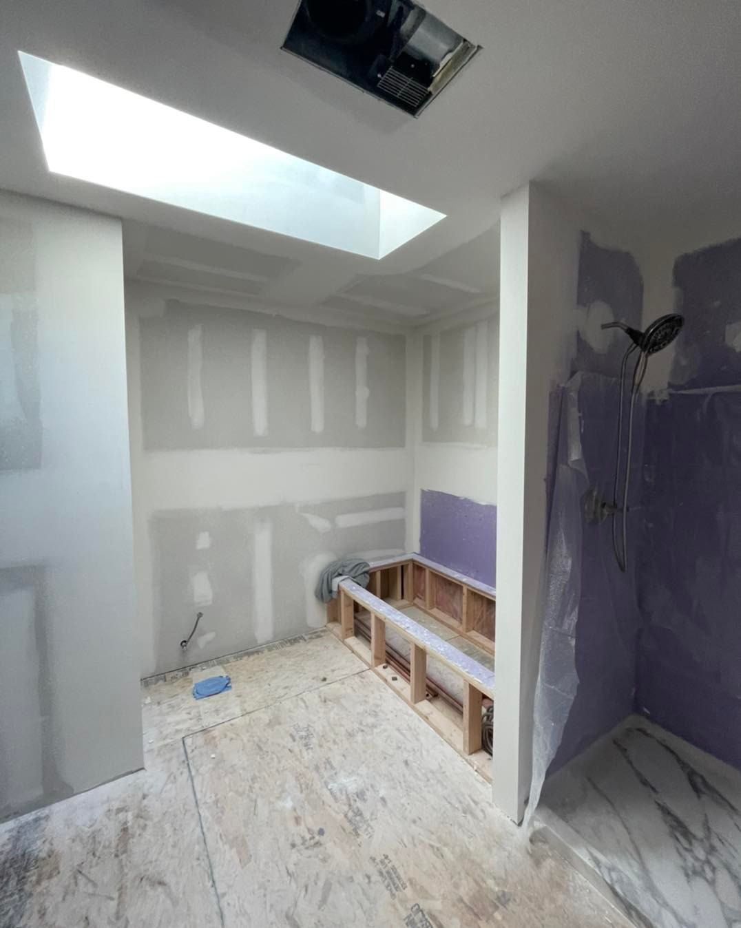 Bathroom remodel in progress with exposed framing and drywall. Sunlight streams from a skylight.