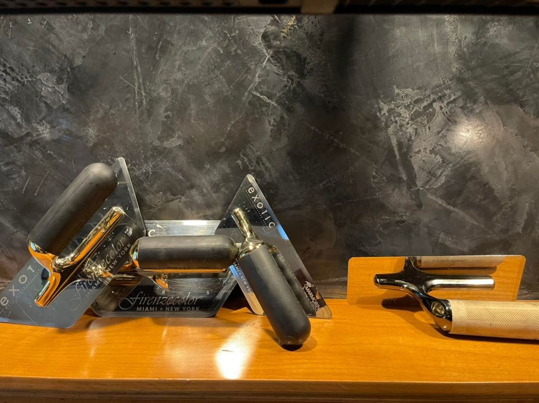 Display of various trowels with black handles against a dark, textured background.