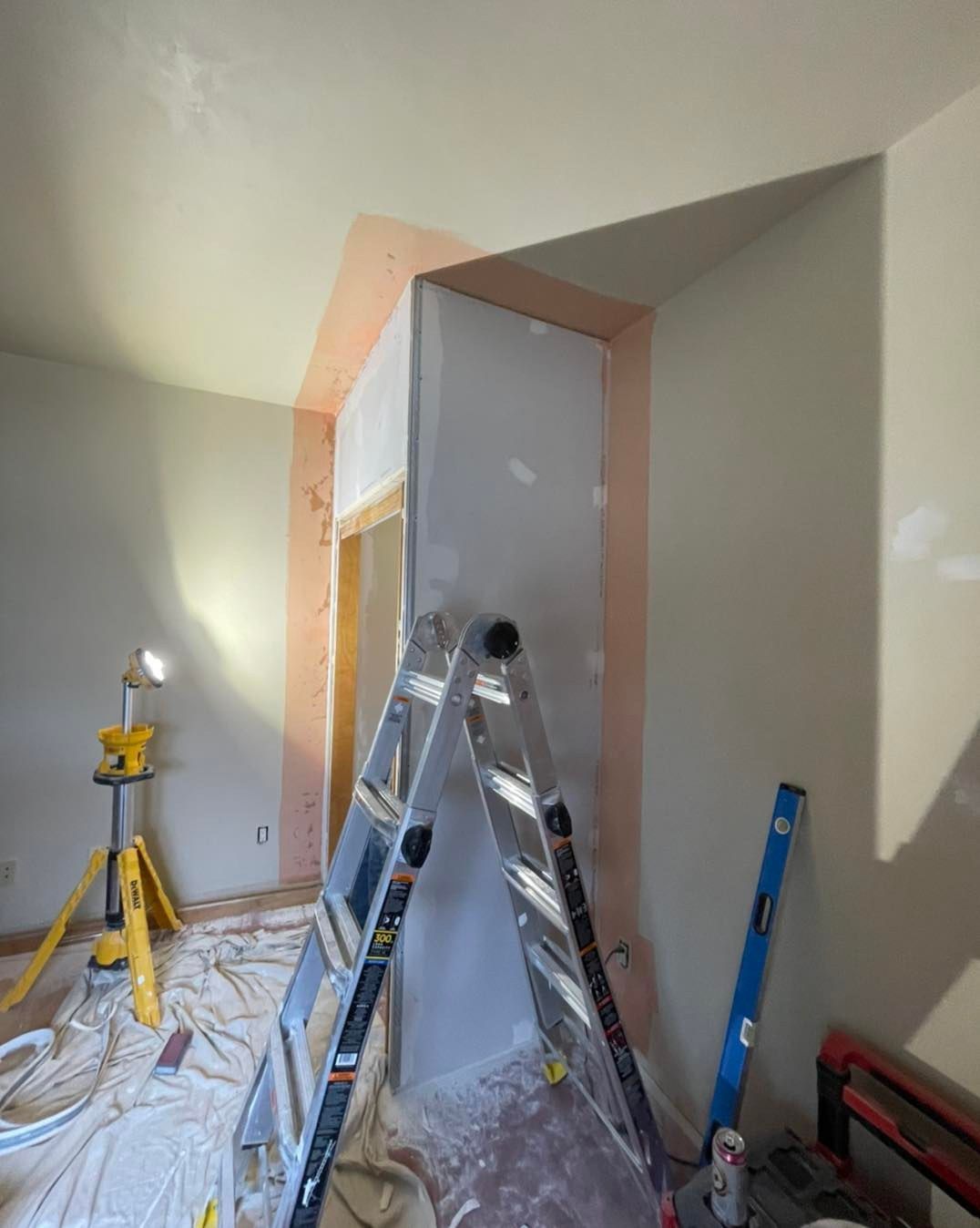 Room under renovation with a ladder, drywall, and a work light.
