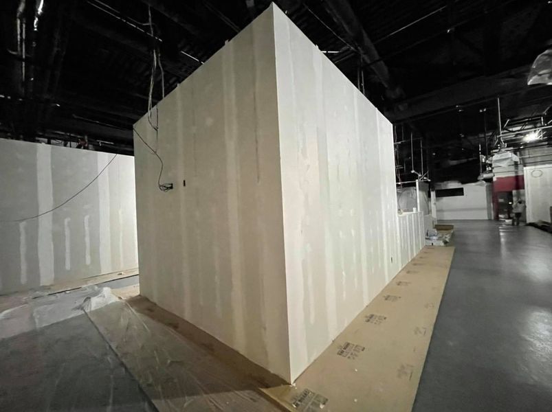 Corner of unfinished walls in a construction space, with exposed wood and drywall.