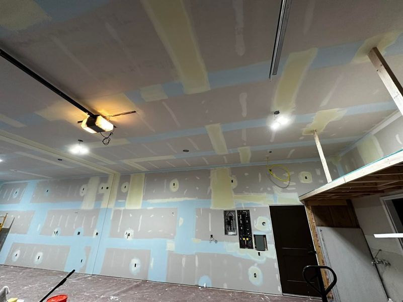 Garage interior with drywall installation, blue taping, and electrical fixtures.