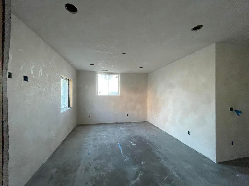 An empty, unfinished room with stucco walls, concrete floor, and small windows, awaiting completion.