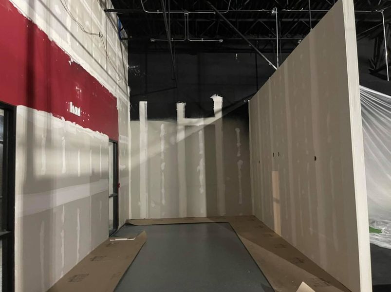 Interior view of a room under construction with drywall walls and red painted accent; gray floor.