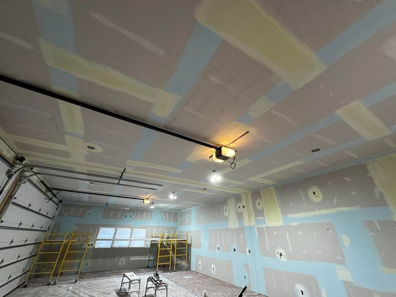Garage interior under construction; drywall and ceiling work in progress with scaffolding and lights.