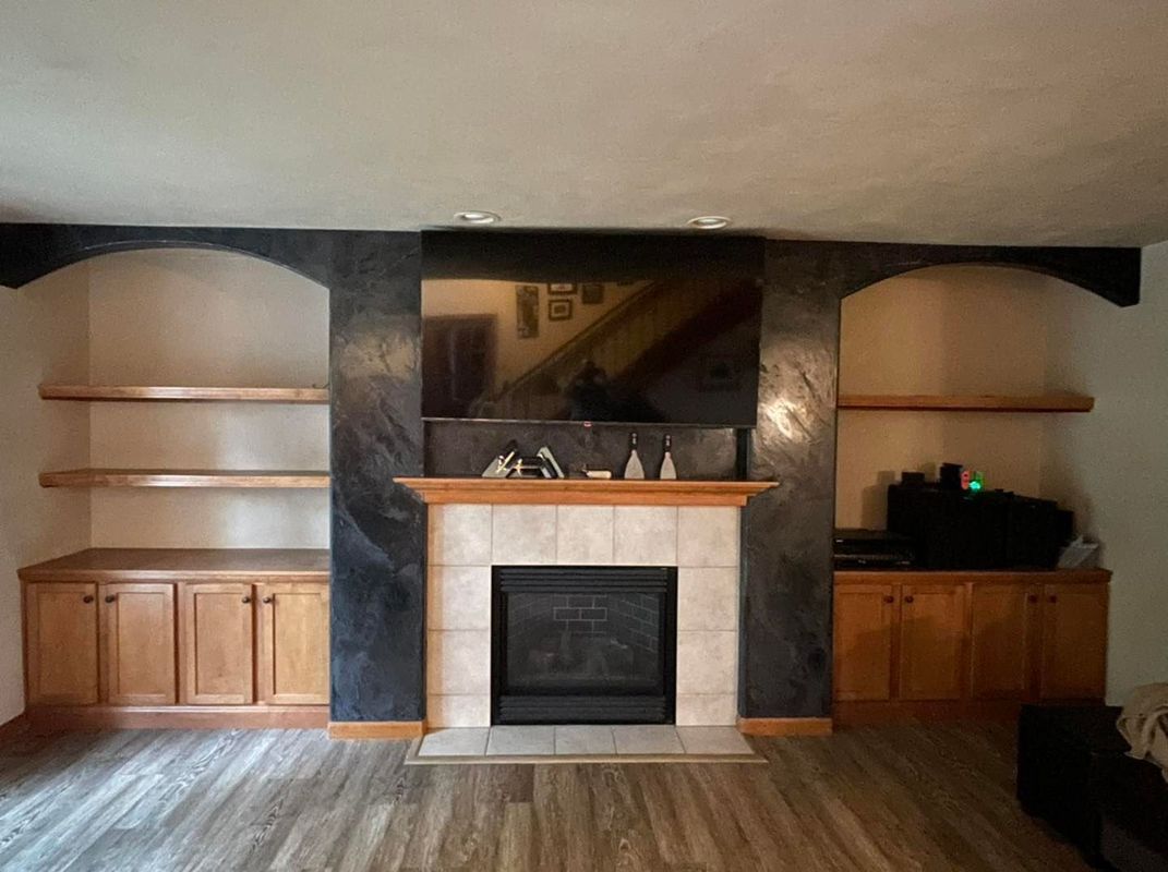 Fireplace with built-in shelves and cabinets. TV above the fireplace, all in a living room with wood floors.