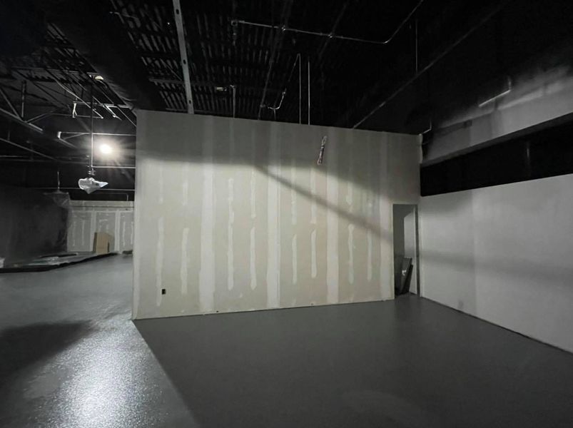 Interior view of a construction site with gray floor, unfinished walls, and black ceiling.