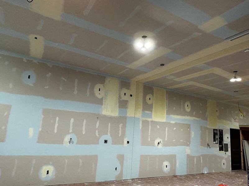 Interior room under construction, with drywall, patches, and exposed wiring.