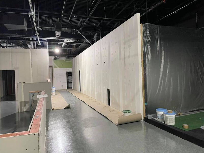 Interior view of a building under construction. A long wall with doorways is visible, and the floor is a light grey color.