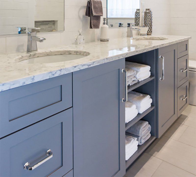 Blue bathroom vanity with white marble countertop, sink, and open towel storage drawers
