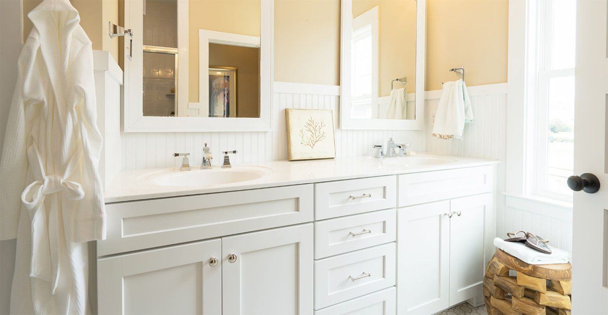 Bright white bathroom vanity with double sinks, mirrors, towels, and a woven basket by the window.