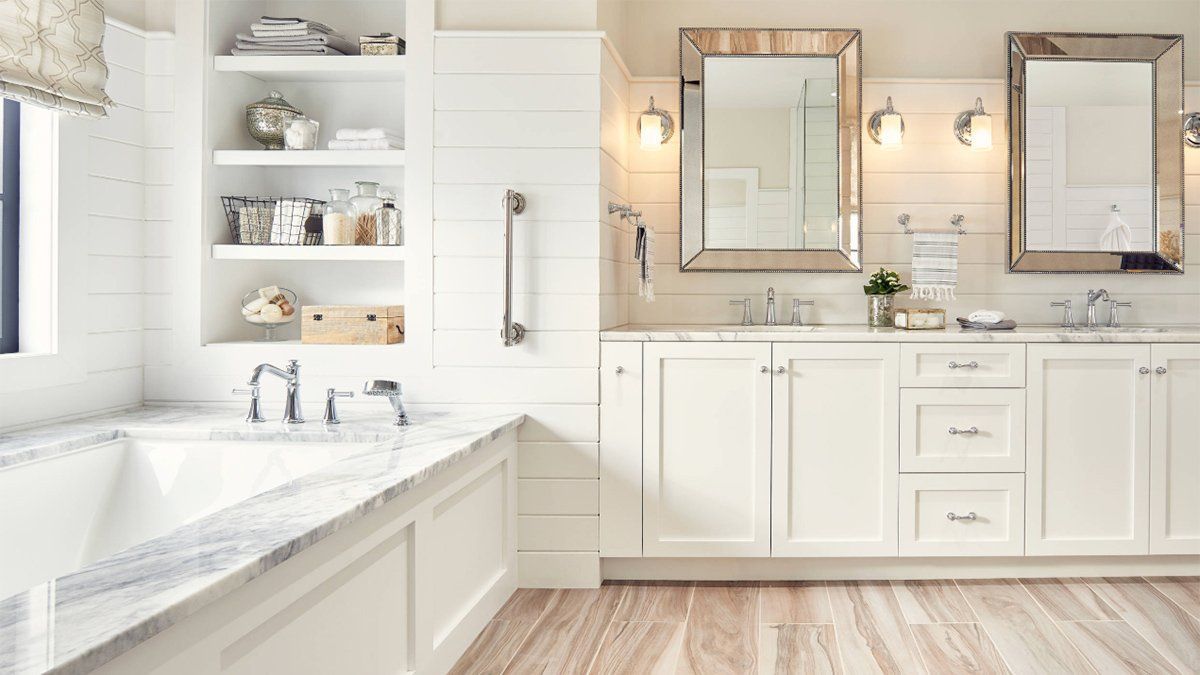 Bright white bathroom with a bathtub, double vanity, wall mirrors, and light wood flooring.