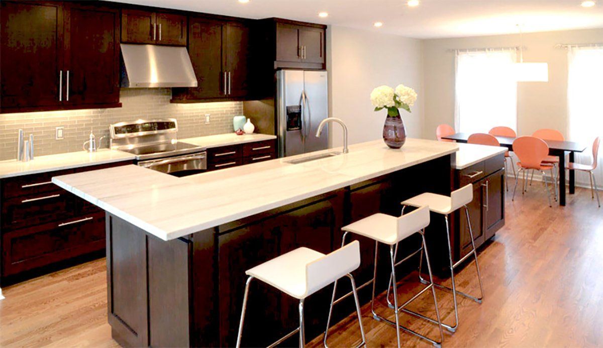 Modern kitchen with a large island, dark cabinets, stainless appliances, and bar stools in an open dining area