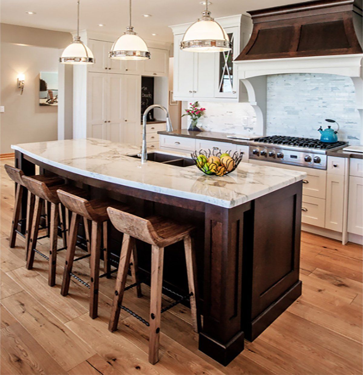 Modern kitchen with a large island, wooden stools, marble counters, and pendant lights
