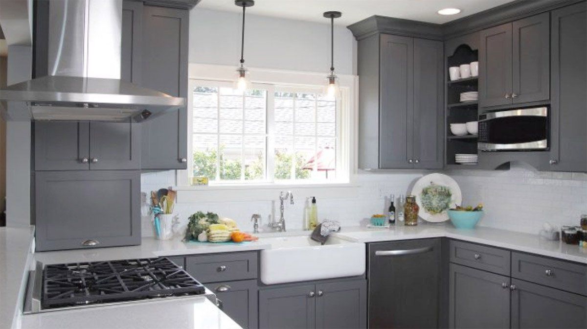 Bright gray kitchen with dark cabinets, white countertops, gas stove, sink, and window over the sink.