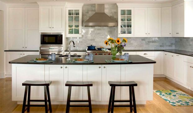 Bright white kitchen with island, three stools, stainless range hood, and sunflowers on the counter