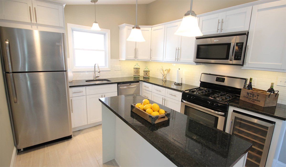 Bright modern kitchen with stainless appliances, white cabinets, and a black island with fruit bowl.