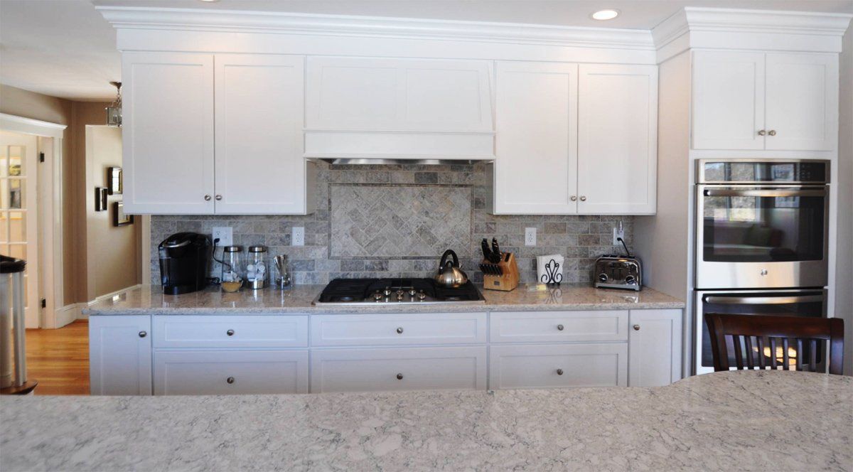 Modern white kitchen with marble countertops, built-in oven, and decorative backsplash.