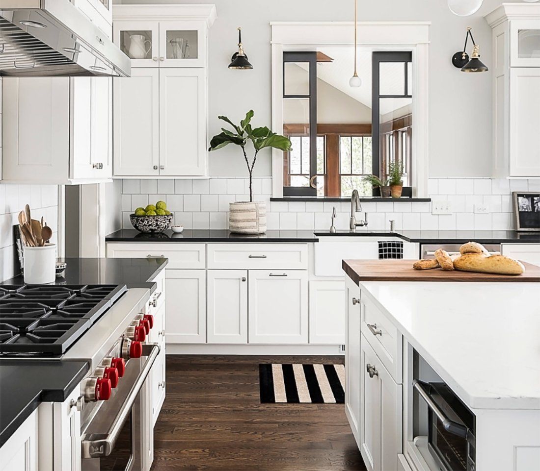 Bright white modern kitchen with black accents, island, stove, and window above the sink