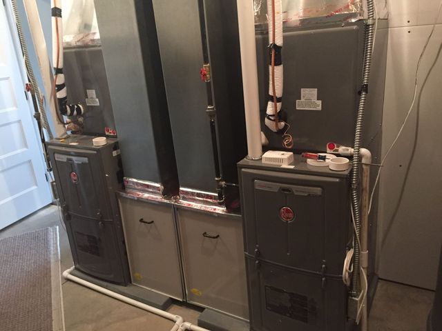 Two gray HVAC units installed in a basement, with associated ductwork and piping.