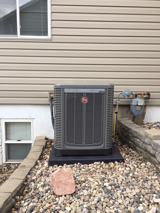 Central air conditioning unit outside a building, on a black base amidst rocks.