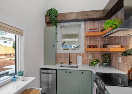 Modern kitchen with green cabinets, wood shelves, black stove, sink, and a window seat by a bright window
