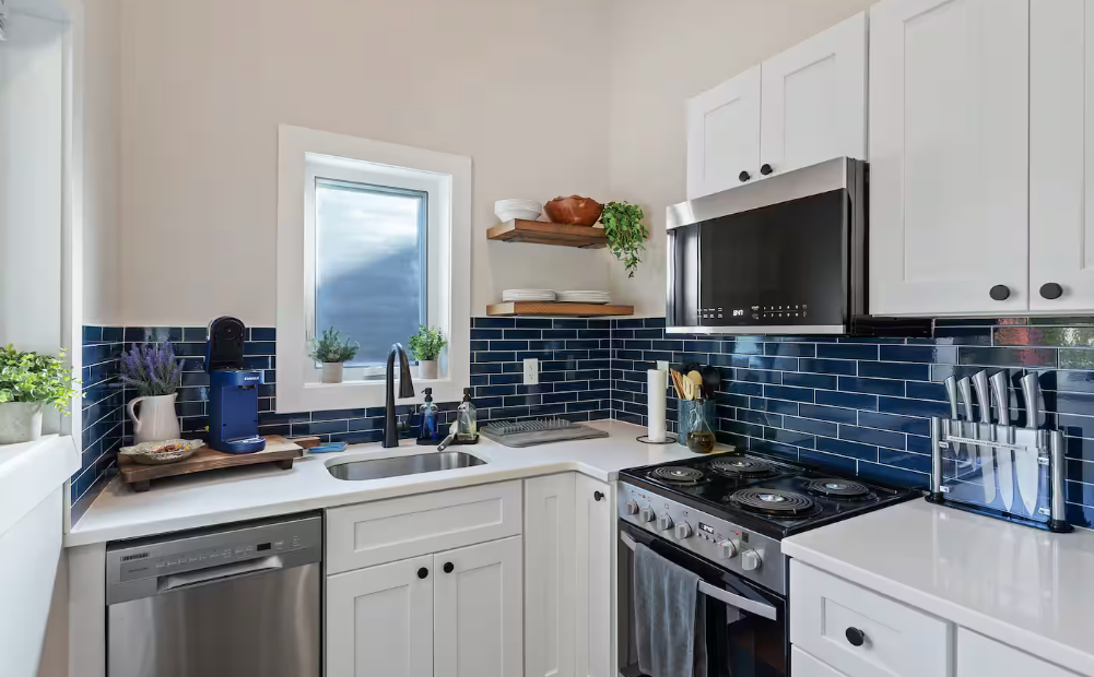 Bright modern kitchen with white cabinets, blue backsplash, and a stainless steel stove and microwave.