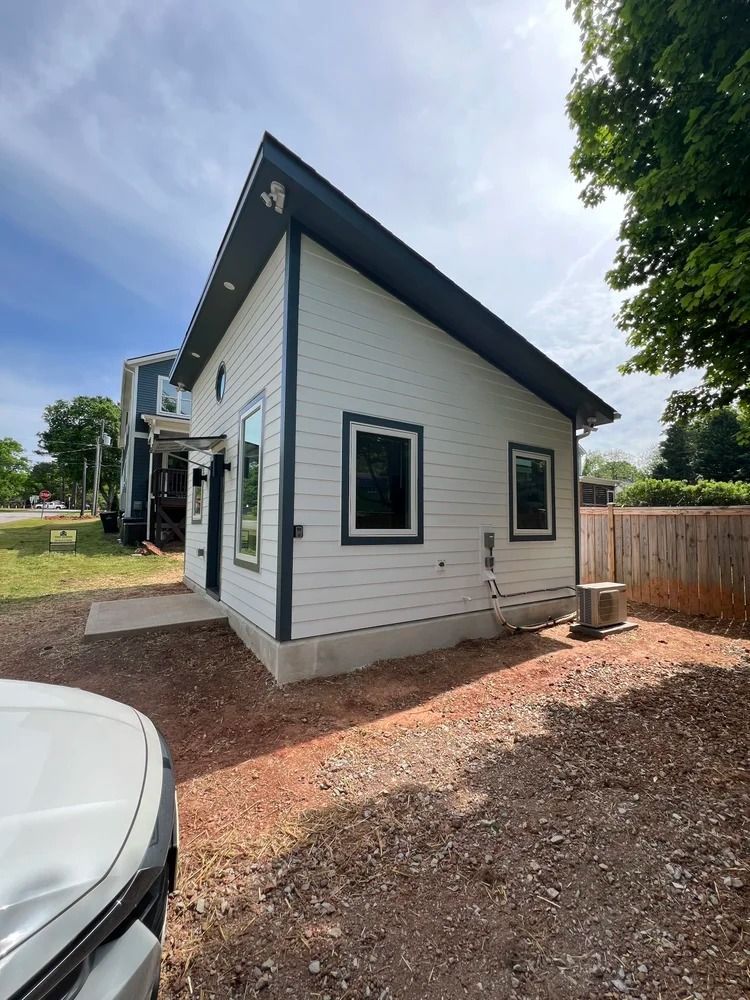 Small white modern house with dark trim, sloped roof, and gravel yard beside a wooden fence.