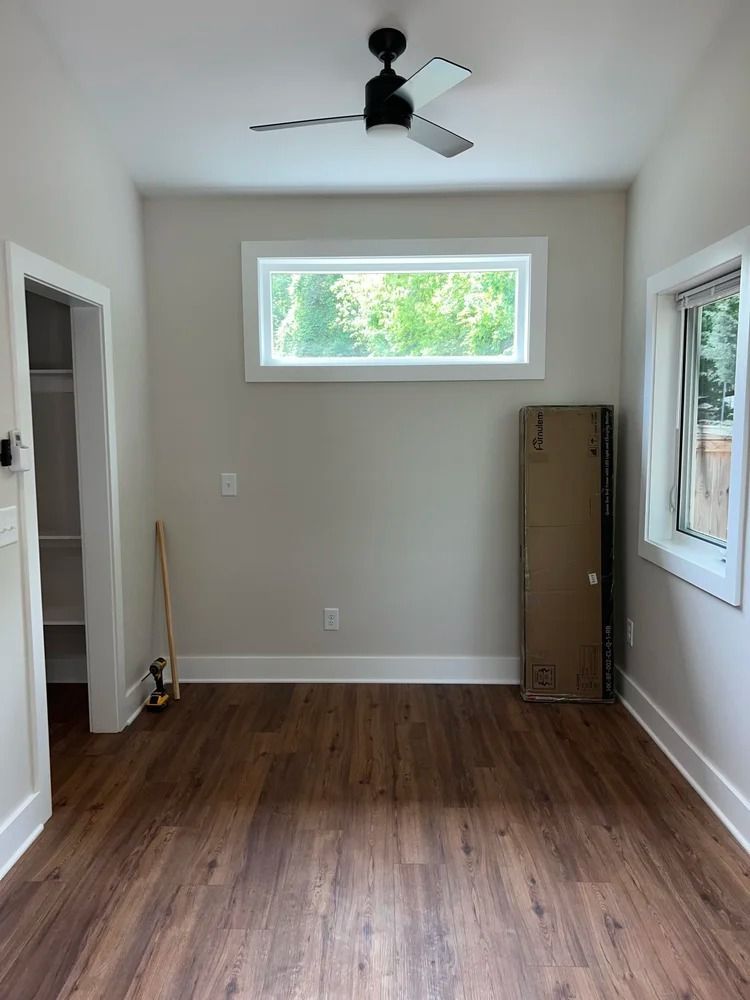 Empty room with wood floors, white walls, two windows, and a ceiling fan.