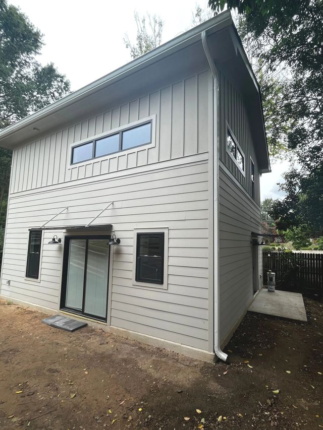 Two-story gray house exterior with large windows and a ground-level sliding glass door surrounded by trees