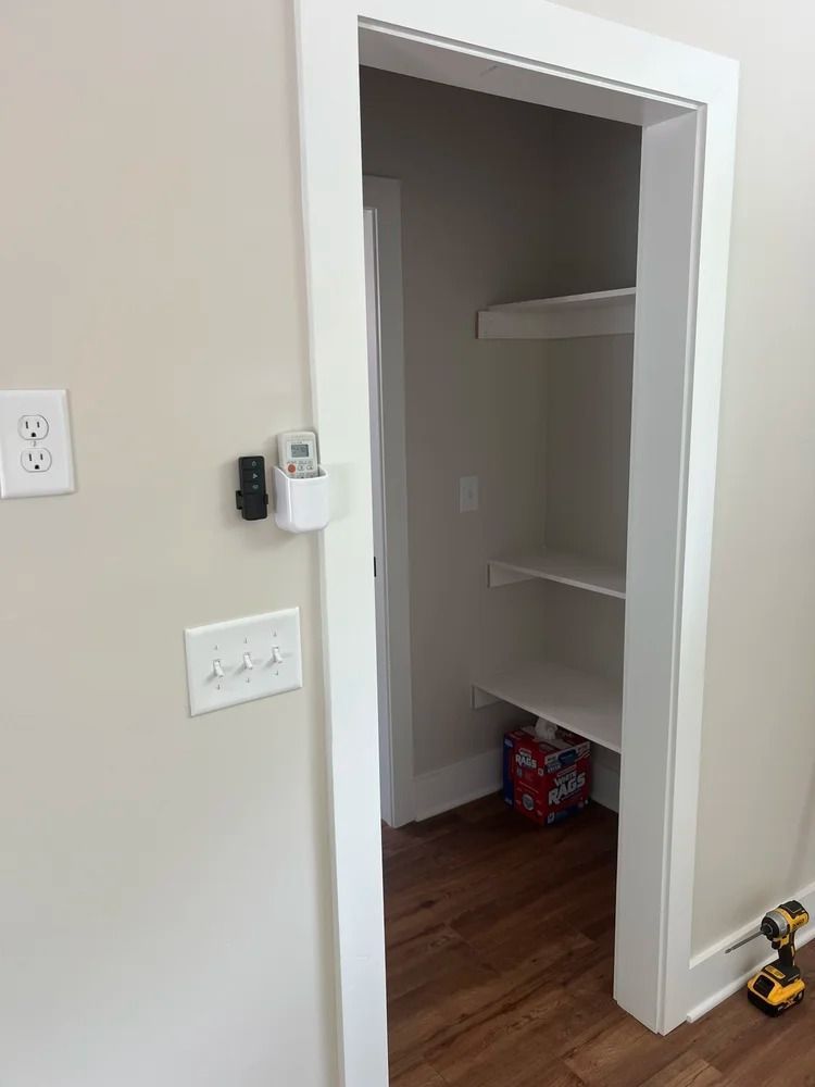 Empty closet with white shelves and wood floor, viewed through a doorway in a beige room.