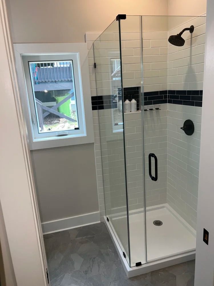 Bathroom with a glass-enclosed shower, white tile, and a small window letting in light.