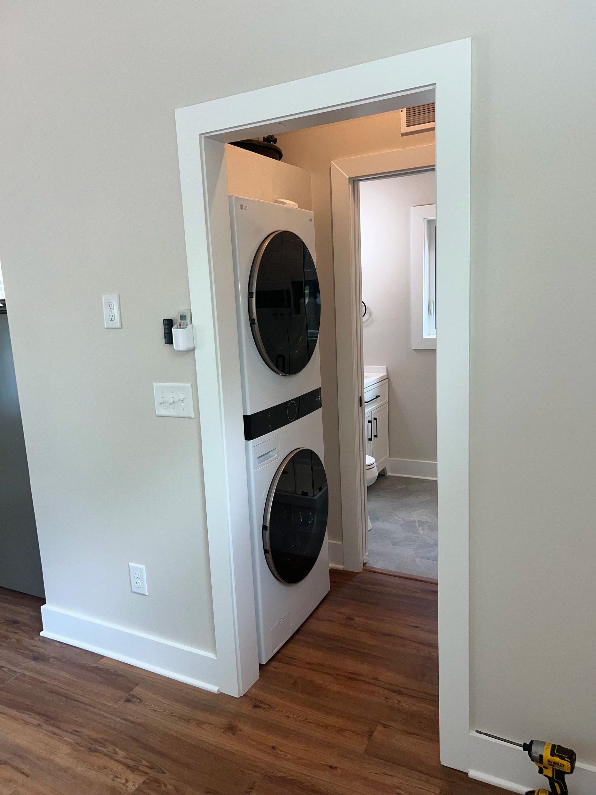Laundry closet with stacked washer and dryer in a white doorway with wood flooring.